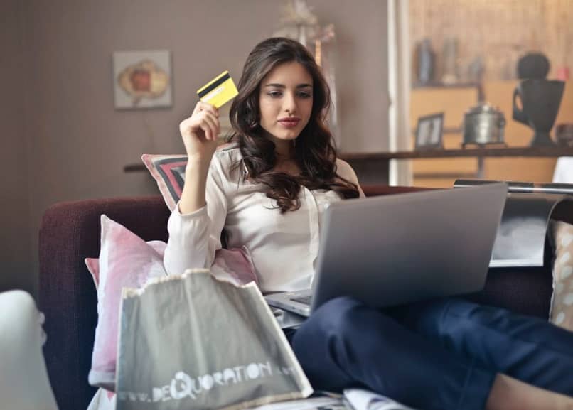 mujer con sus compras y la laptop usando la tarjeta de crédito