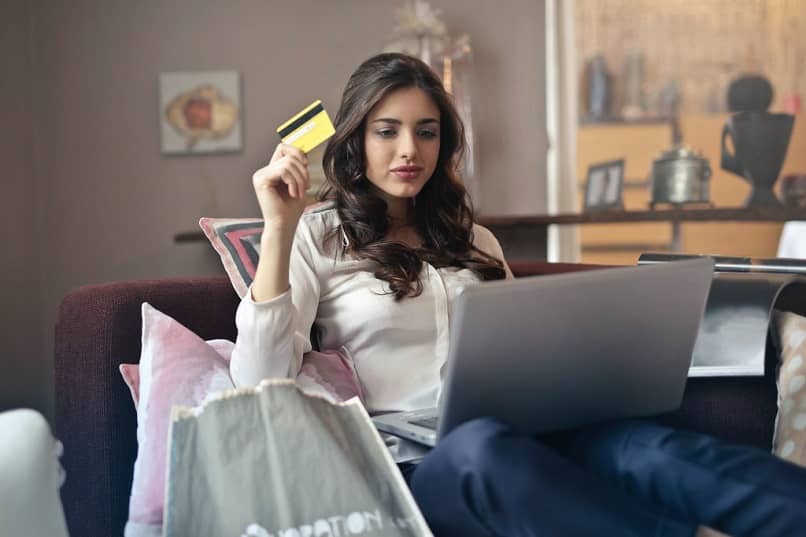 mujer en el sofá usando la laptop con bolsas de compras y tarjeta de crédito en la mano