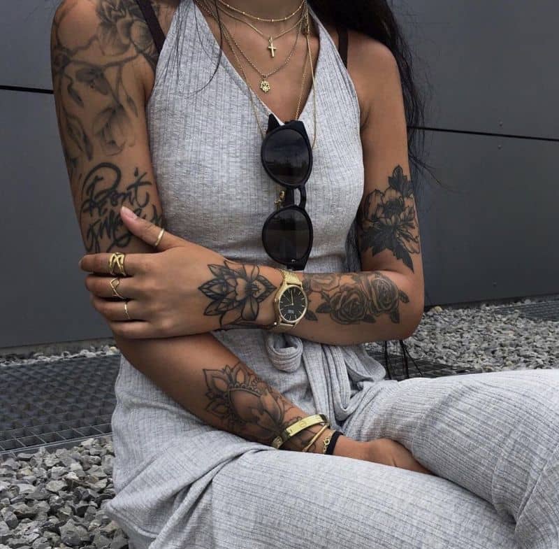 Mujer tatuada con prenda gris sentada 