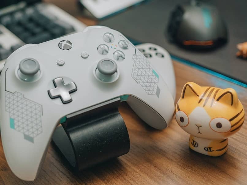 mando de videojuegos marca xboxlive blanco en escritorio junto a muñequeo de gato con rayas