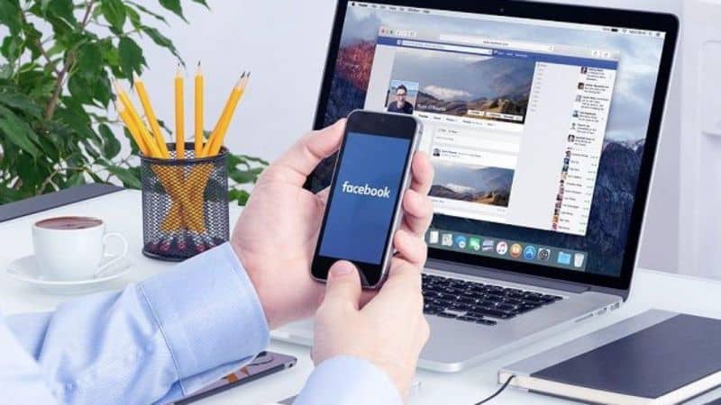 laptop con facebook y manos en movil con facebook lapices y libreta