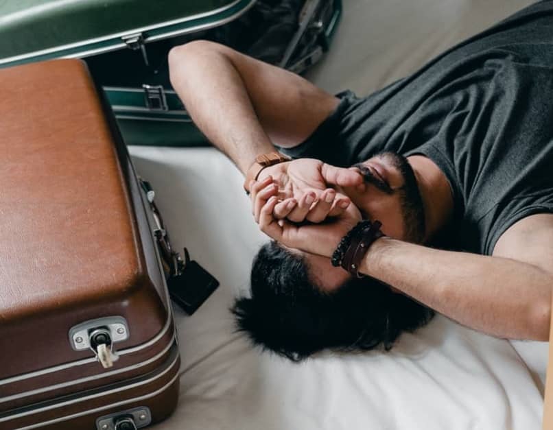 man with arms over his face lying next to suitcase